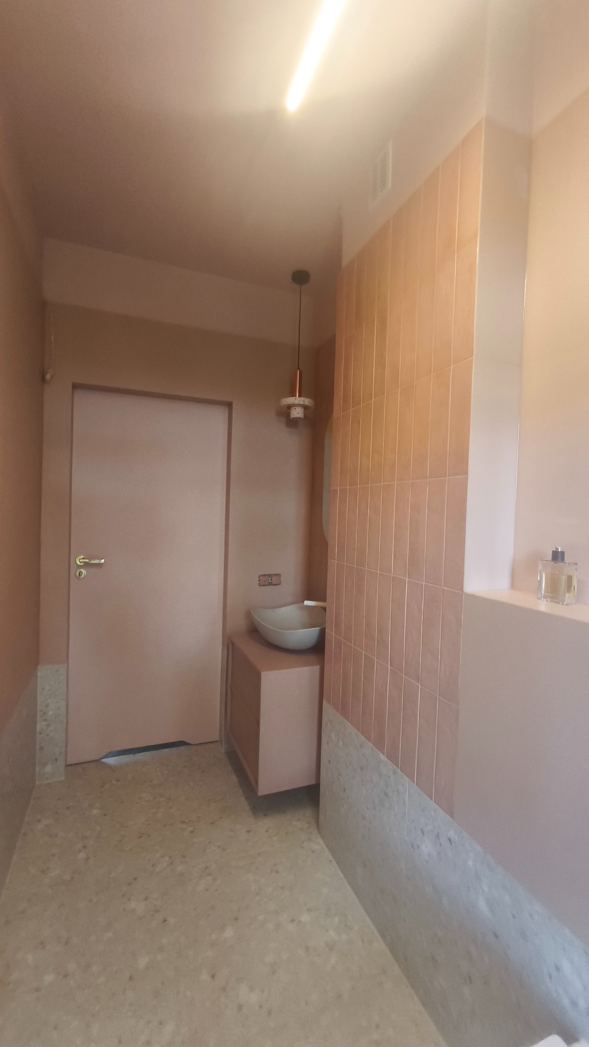 Ukończona łazienka w odcieniach różu: płytki na ścianie, umywalka na szafce, podłoga z lastryko. Minimalistyczny design, nowoczesne oświetlenie.