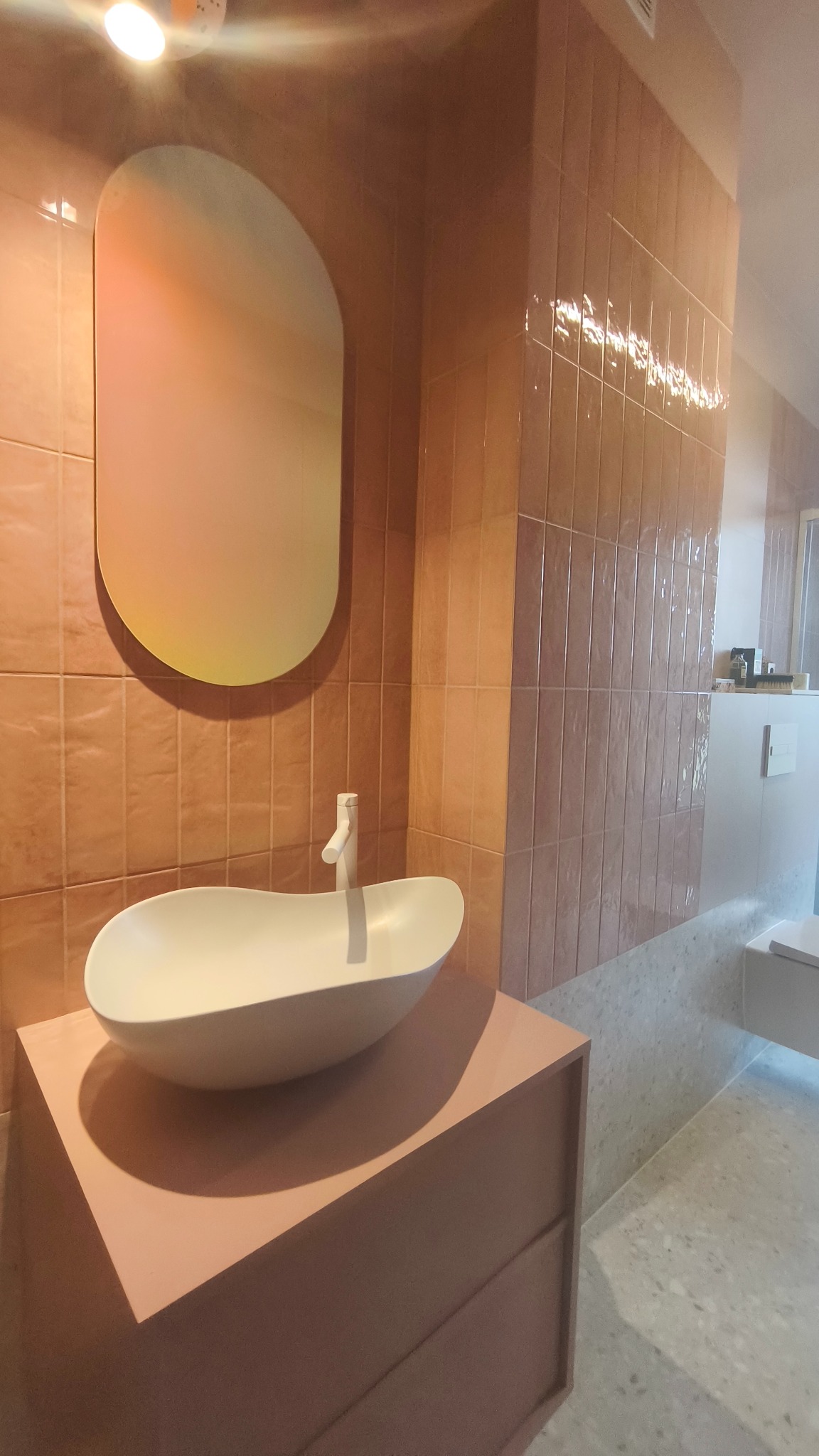 Nowoczesna łazienka w odcieniach różu: owalne lustro, umywalka na szafce i pionowe płytki. Minimalistyczny design z dbałością o detale.