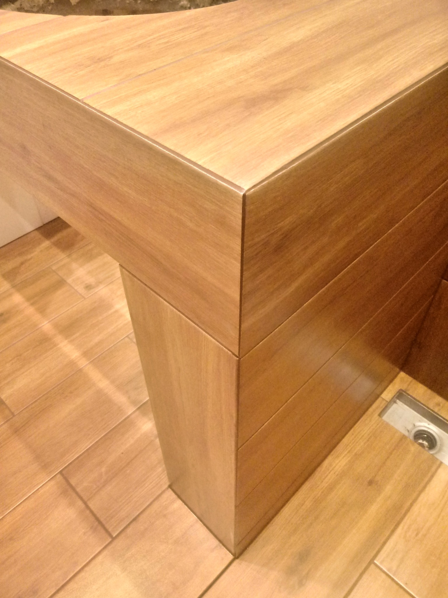 Detal wykończenia łazienki: drewnopodobna umywalka z blatem i odpływem liniowym w podłodze wyłożonej płytkami imitującymi drewno.