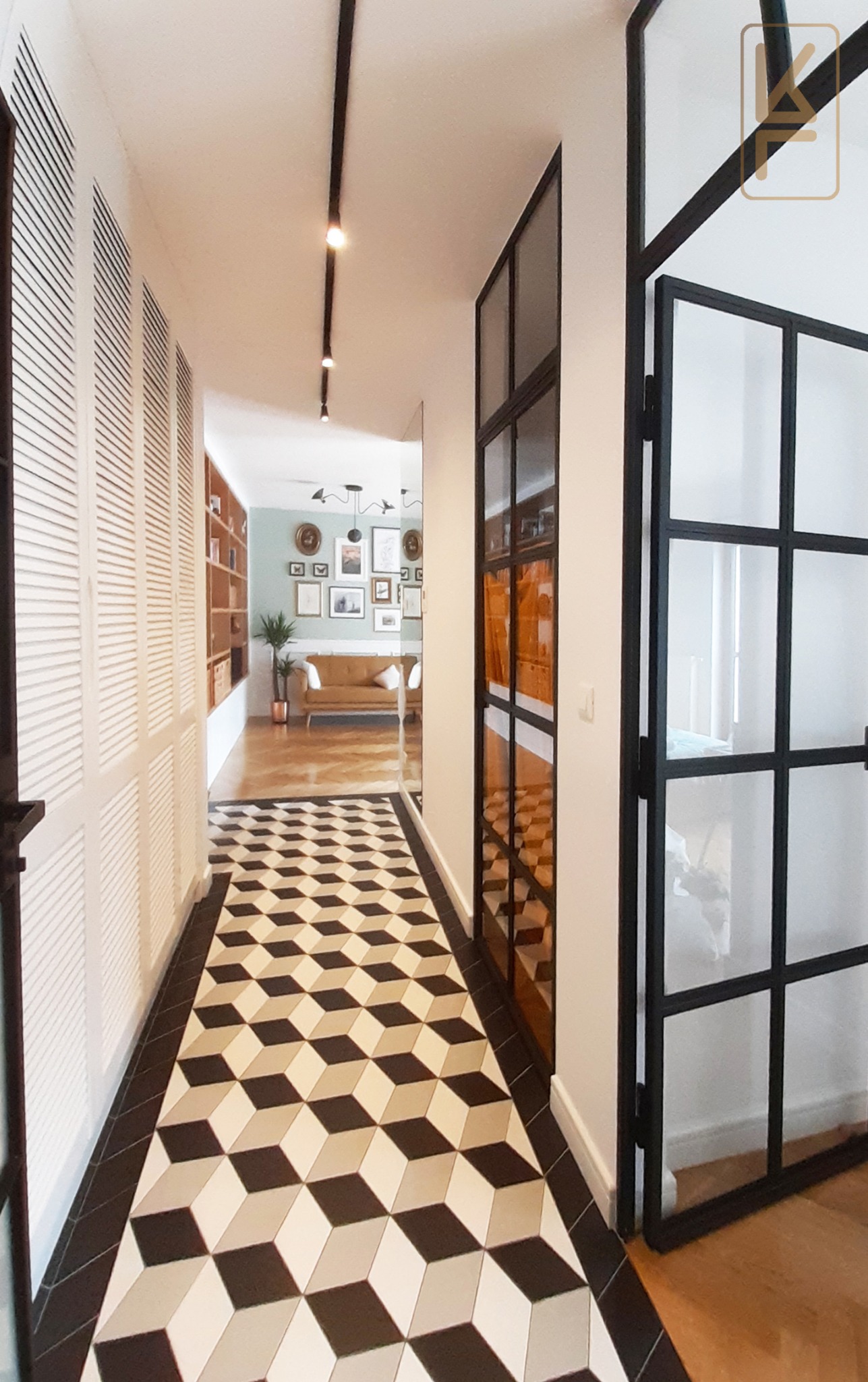 Korytarz z podłogą w geometryczny wzór 3D, białe szafy z żaluzjowymi drzwiami po lewej, przeszklone drzwi w czarnej ramie po prawej, widok na salon z sofą i galerią obrazów.