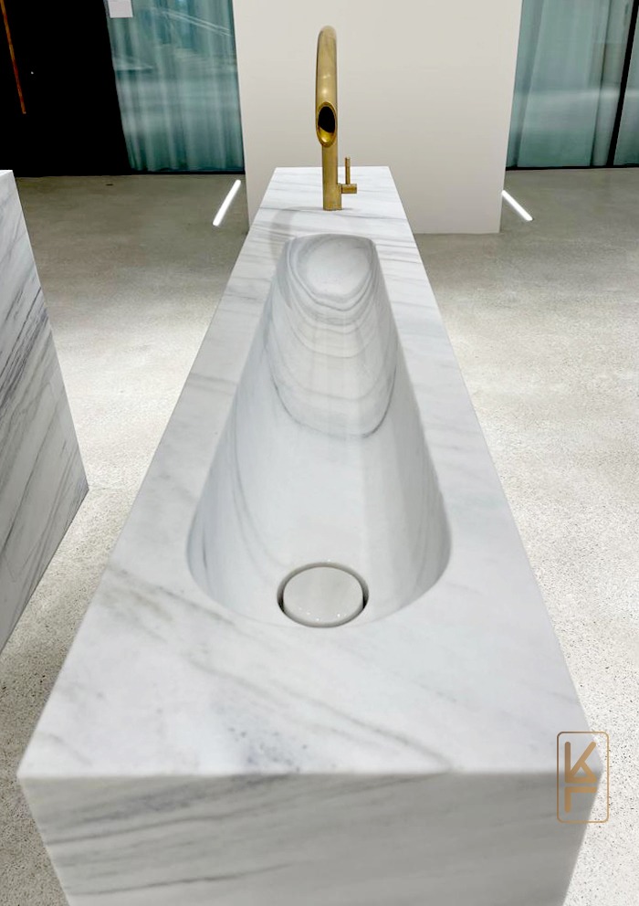 Nowoczesna umywalka z białego marmuru z oryginalną, złotą baterią w minimalistycznym wnętrzu.
