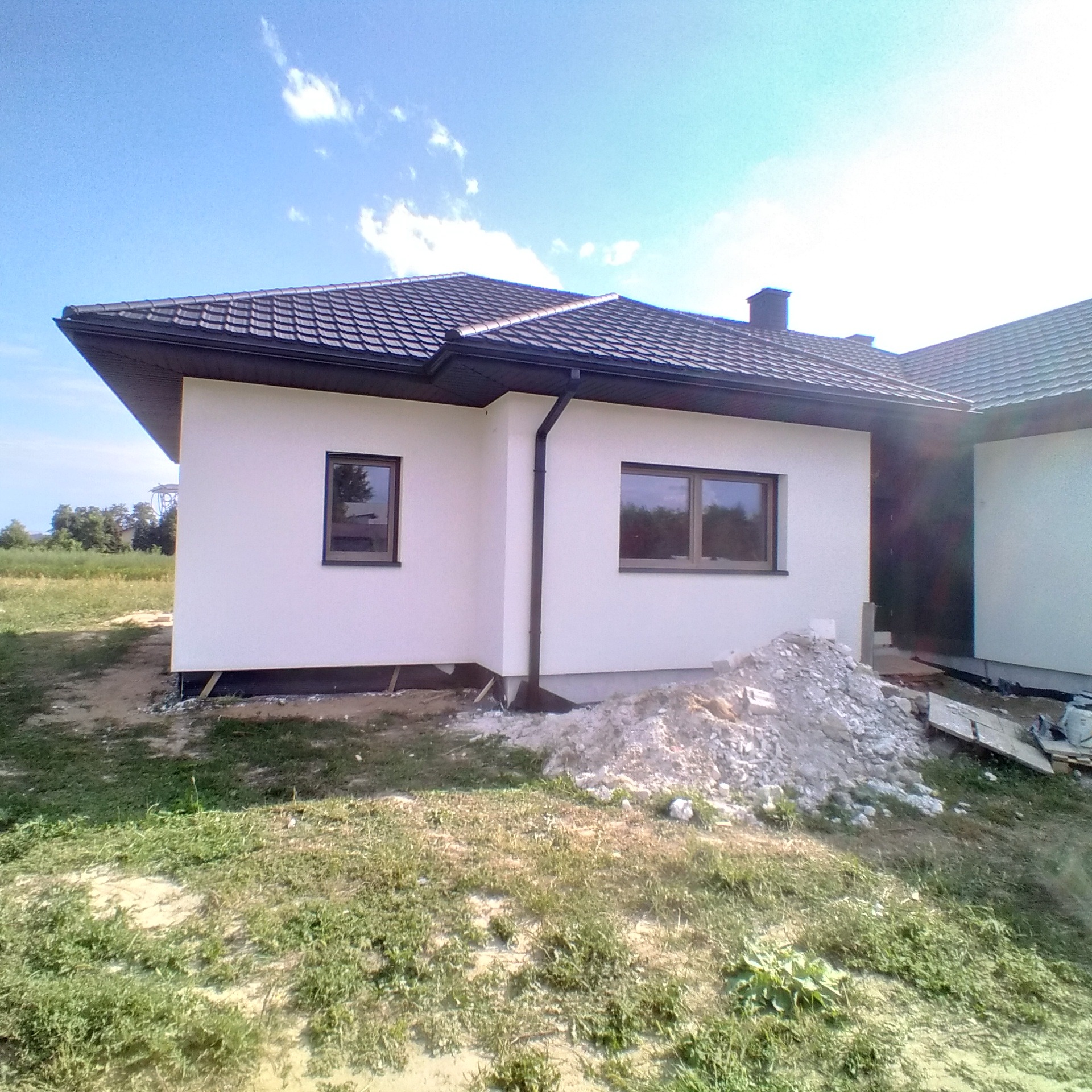 Nowo otynkowany dom w Dubiecku z brązowymi oknami i ciemnym dachem z dachówki, widoczny stos gruzu.