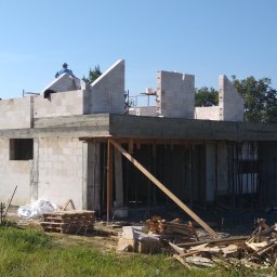 Mk bud - Wznoszenie dwukondygnacyjnego budynku z betonu komórkowego, widoczny pracownik na dachu i drewniane stemple podtrzymujące strop.