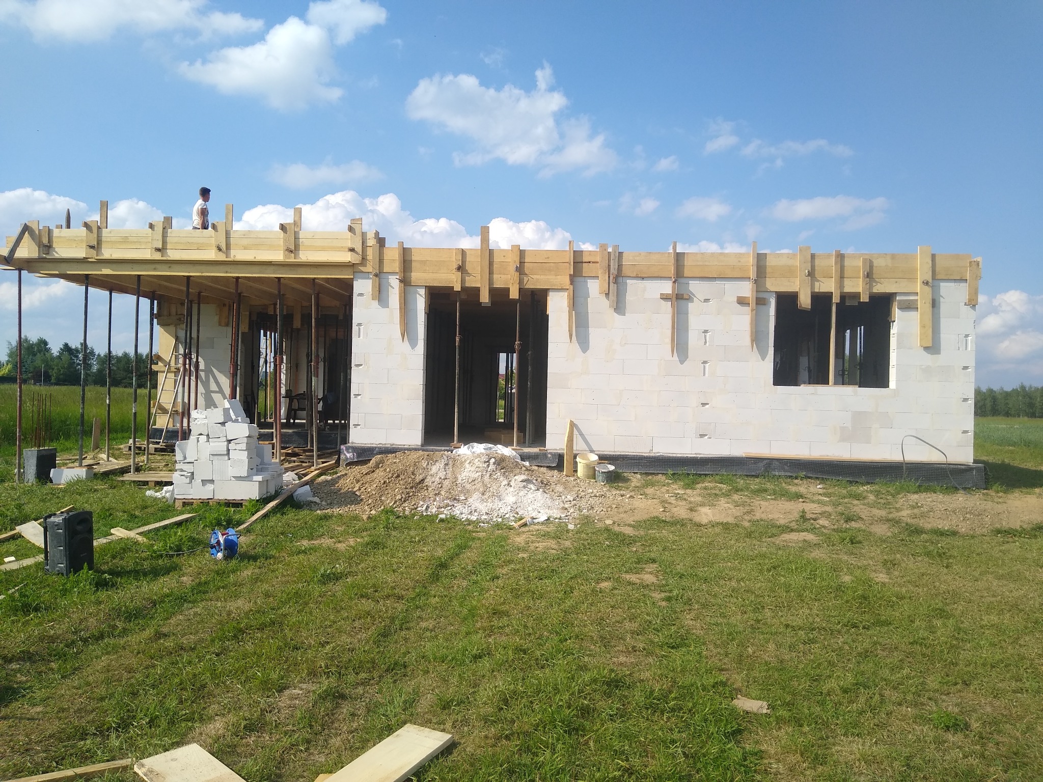 Wznoszenie ścian domu z betonu komórkowego, widoczne drewniane szalunki stropu i podpory, na górze budynku stoi pracownik.