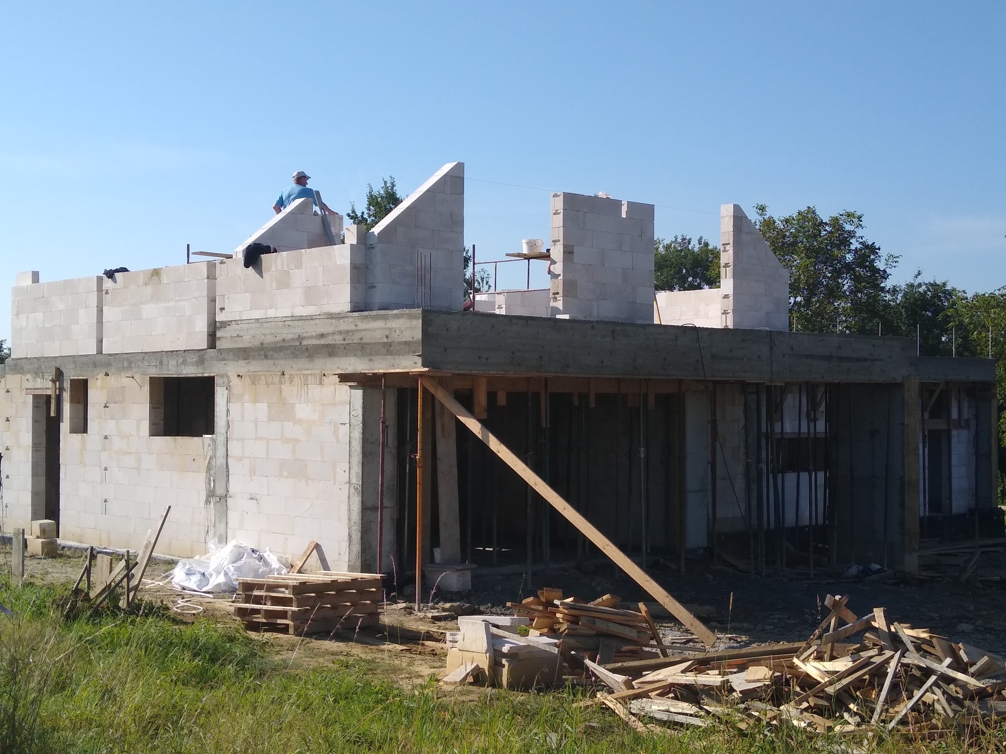 Wznoszenie dwukondygnacyjnego budynku z betonu komórkowego, widoczny pracownik na dachu i drewniane stemple podtrzymujące strop.