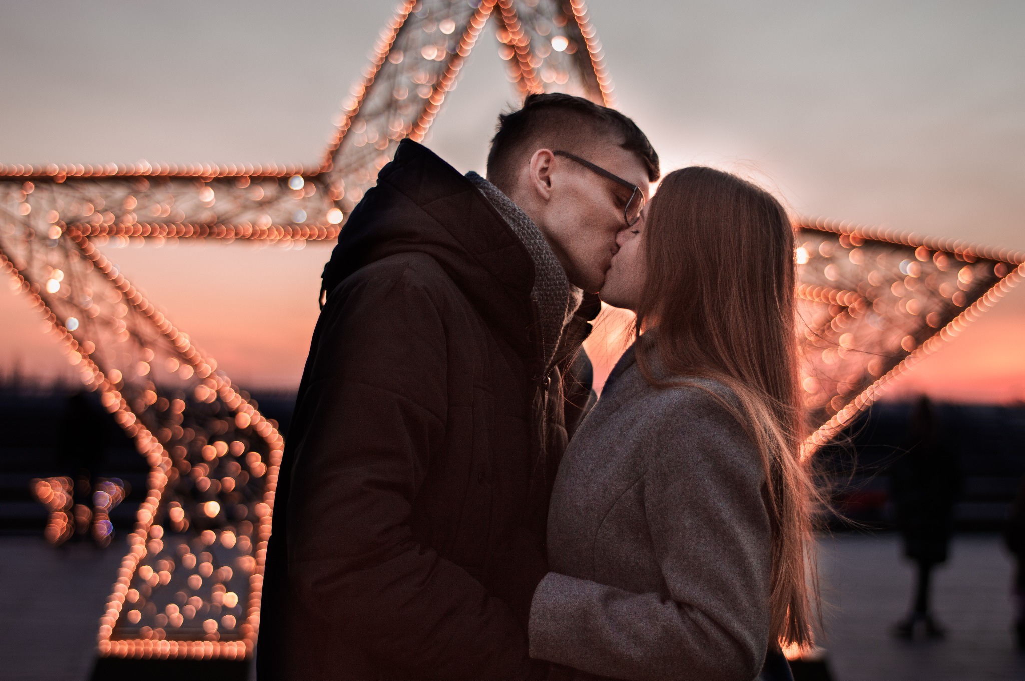 Para całująca się na tle dużej gwiazdy z lampek podczas wieczornego wydarzenia plenerowego.