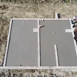 Zalany fundament pod budynek z widocznymi elementami instalacji i ekipą budowlaną, ujęcie z góry.