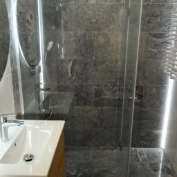 EURO-MIX PIOTR KWAŚNIEWSKI - Nowoczesna łazienka z szarymi płytkami imitującymi kamień, kabiną prysznicową typu walk-in i umywalką z szafką w kolorze drewna. Widoczne oświetlenie LED.