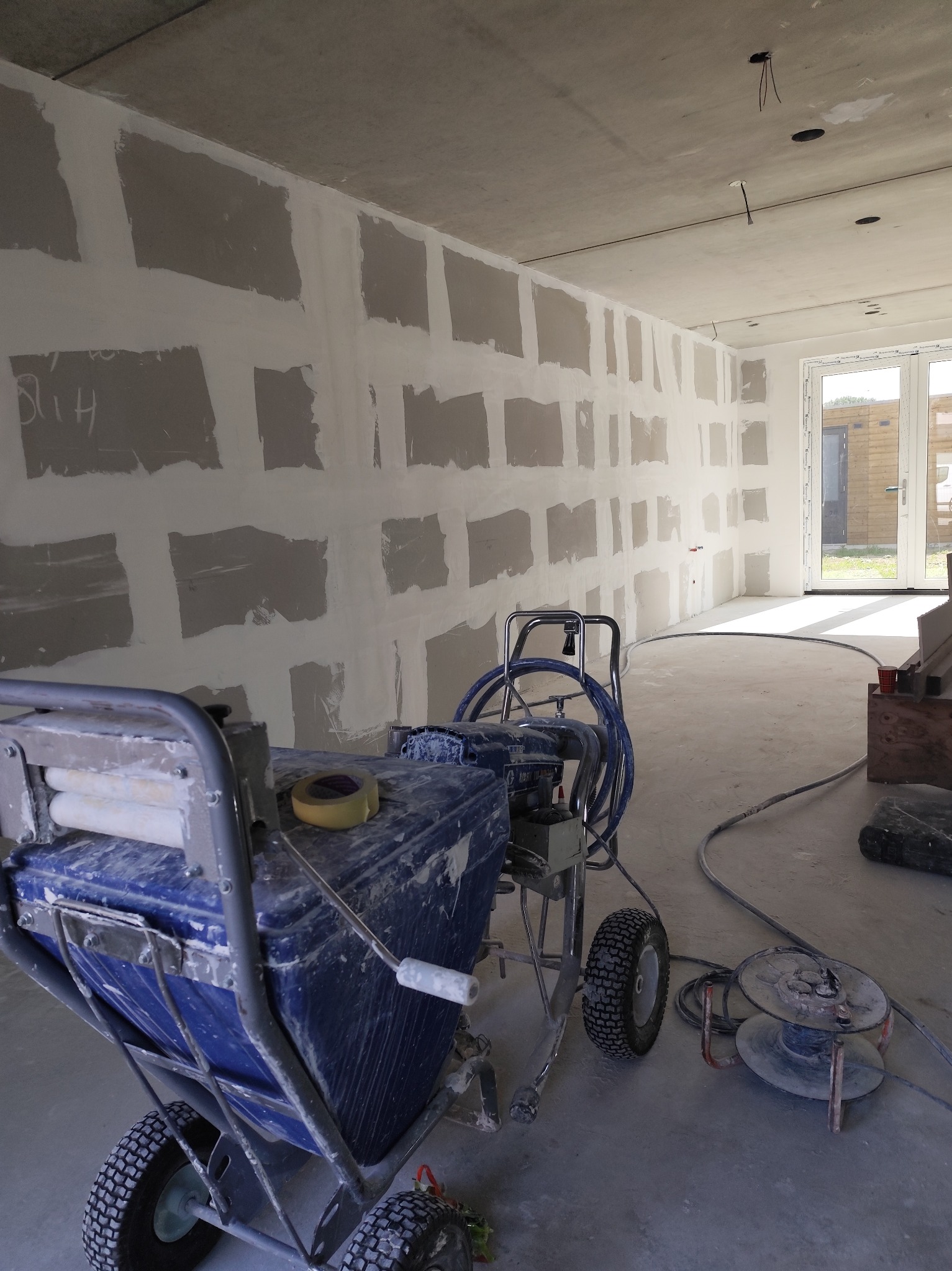 Pokój w trakcie szpachlowania, widoczna szpachlownica ciśnieniowa, ściany z płyt karton-gips, gotowe do dalszej obróbki, z widocznymi łączeniami płyt.