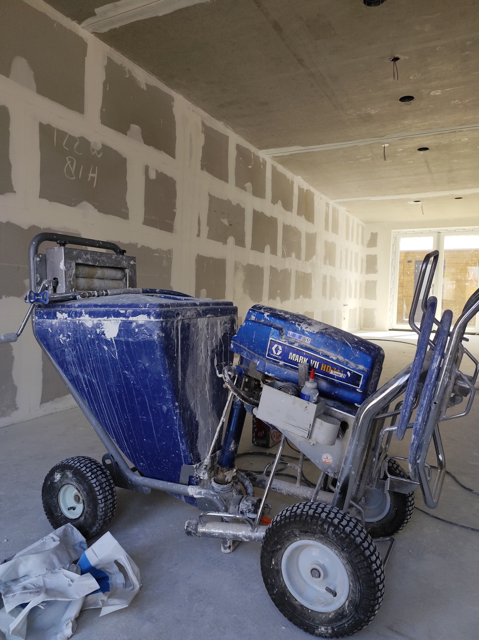 Agregat malarski Graco Mark VII HD na tle surowych ścian z płyt karton-gips, przygotowanych do dalszych prac wykończeniowych. Widoczne instalacje elektryczne w suficie.