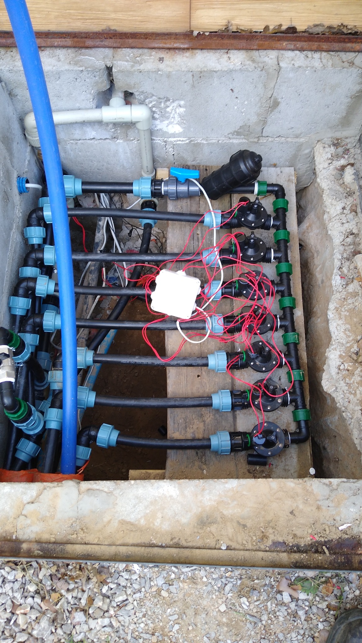 System nawadniania z rurami, zaworami i okablowaniem, umieszczony w betonowej skrzynce, widoczne elementy instalacji podziemnej.