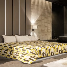 Sebastian Drelichowski - Nowoczesna sypialnia z łazienką en suite. Uwagę przykuwają dekoracyjne panele ścienne, geometryczna narzuta na łóżko i wolnostojąca wanna w ciemnej tonacji.