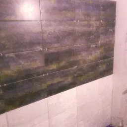 Ściana w trakcie wykańczania z dwukolorowymi płytkami: górna część w odcieniach fioletu i zieleni, dolna w kolorze białym, widoczne krzyżyki dystansowe między płytkami.