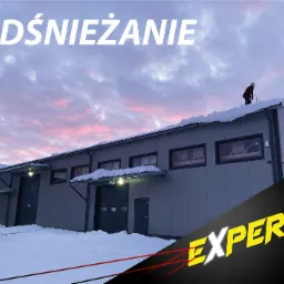 Pracownik w czerwonej kurtce odśnieża dach dużego, szarego budynku przemysłowego o zmierzchu, na tle różowego nieba. Widoczne zaspy śniegu przed budynkiem i logo firmy w rogu.