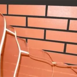 Fragment ściany z cegieł klinkierowych w kolorze terakoty, z widocznym białym stelażem mocującym, prawdopodobnie przygotowanym do montażu sufitu napinanego.