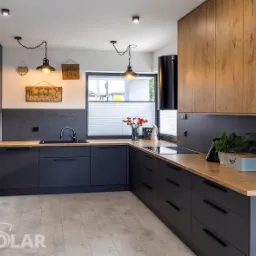 Nowoczesna kuchnia w odcieniach szarości i drewna z wiszącymi lampami w stylu industrialnym, drewnianym blatem i dekoracjami ściennymi.