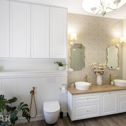 Stolar Group Rafał Kryger - Jasna łazienka z białymi szafkami pod umywalkami, drewnianym blatem, dekoracyjną tapetą, złotą armaturą i wiszącymi szafkami na ścianie.