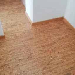 Korkowa podłoga ułożona w korytarzu z białymi ścianami i listwami przypodłogowymi w kolorze drewna.