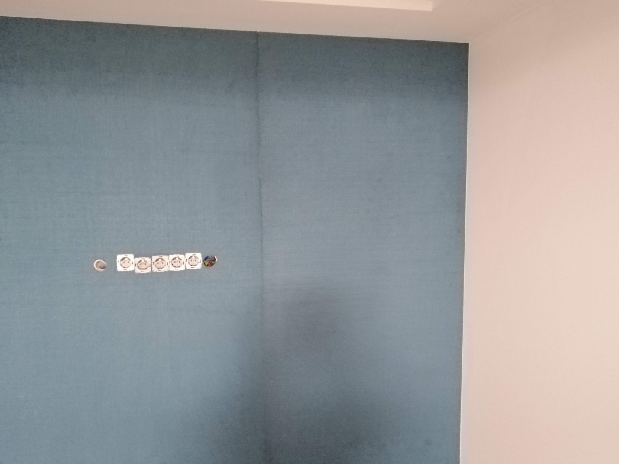 Ściana pomalowana na niebiesko-szaro z widocznymi otworami po gniazdkach elektrycznych, przygotowana do montażu osprzętu.