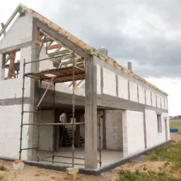 Surowy stan domu z pustaków w Skrzeszewie żukowskim, z widocznym szkieletem dachu i rusztowaniem. W tle pochmurne niebo.