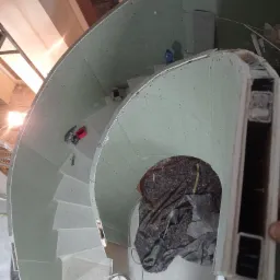 Spiralne schody w trakcie obudowy płytami kartonowo-gipsowymi, widok z góry, z widocznymi narzędziami i fragmentami konstrukcji.