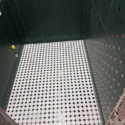 Wykończona łazienka z ciemnozielonymi płytkami ściennymi z dekoracyjnym wzorem i podłogą w biało-czarną szachownicę z ośmiokątnych płytek, widok z góry na wnętrze w trakcie prac.