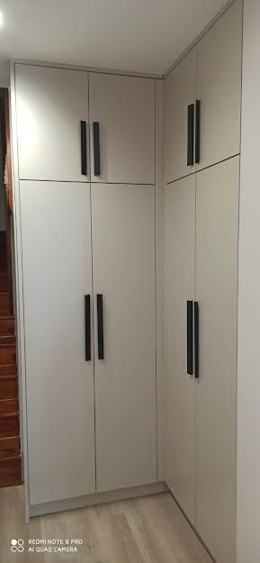 Jasnoszara szafa wnękowa z czarnymi, pionowymi uchwytami, widoczna część schodów w tle.