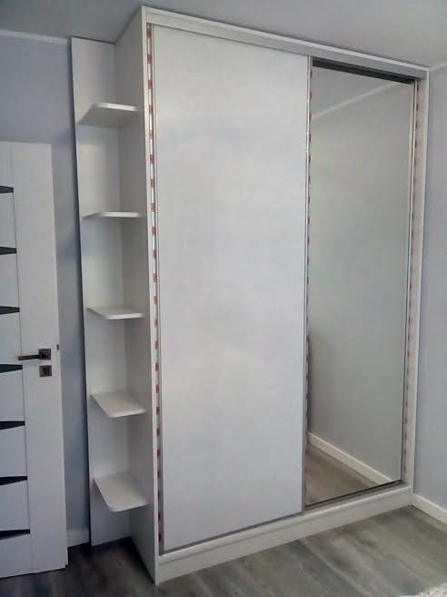 Biała szafa przesuwna z lustrem i półkami bocznymi, widok z boku, minimalistyczny design, szare panele podłogowe.