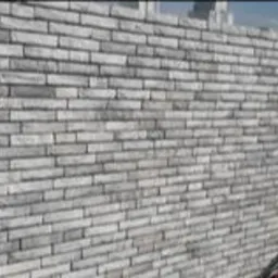 Ściana wykończona szarą cegłą klinkierową, widok z dołu, fragment dachu w prawym dolnym rogu.