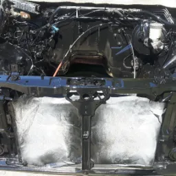 Wnętrze komory silnika samochodu po renowacji, świeżo pomalowane na czarno z widocznymi elementami instalacji i osprzętu, zabezpieczone folią malarską.