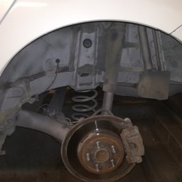 Filtum - Widok na odsłonięte nadkole samochodu z widocznym zawieszeniem, sprężyną i tarczą hamulcową z zaciskiem, po prawdopodobnym oczyszczeniu i zabezpieczeniu antykorozyjnym.