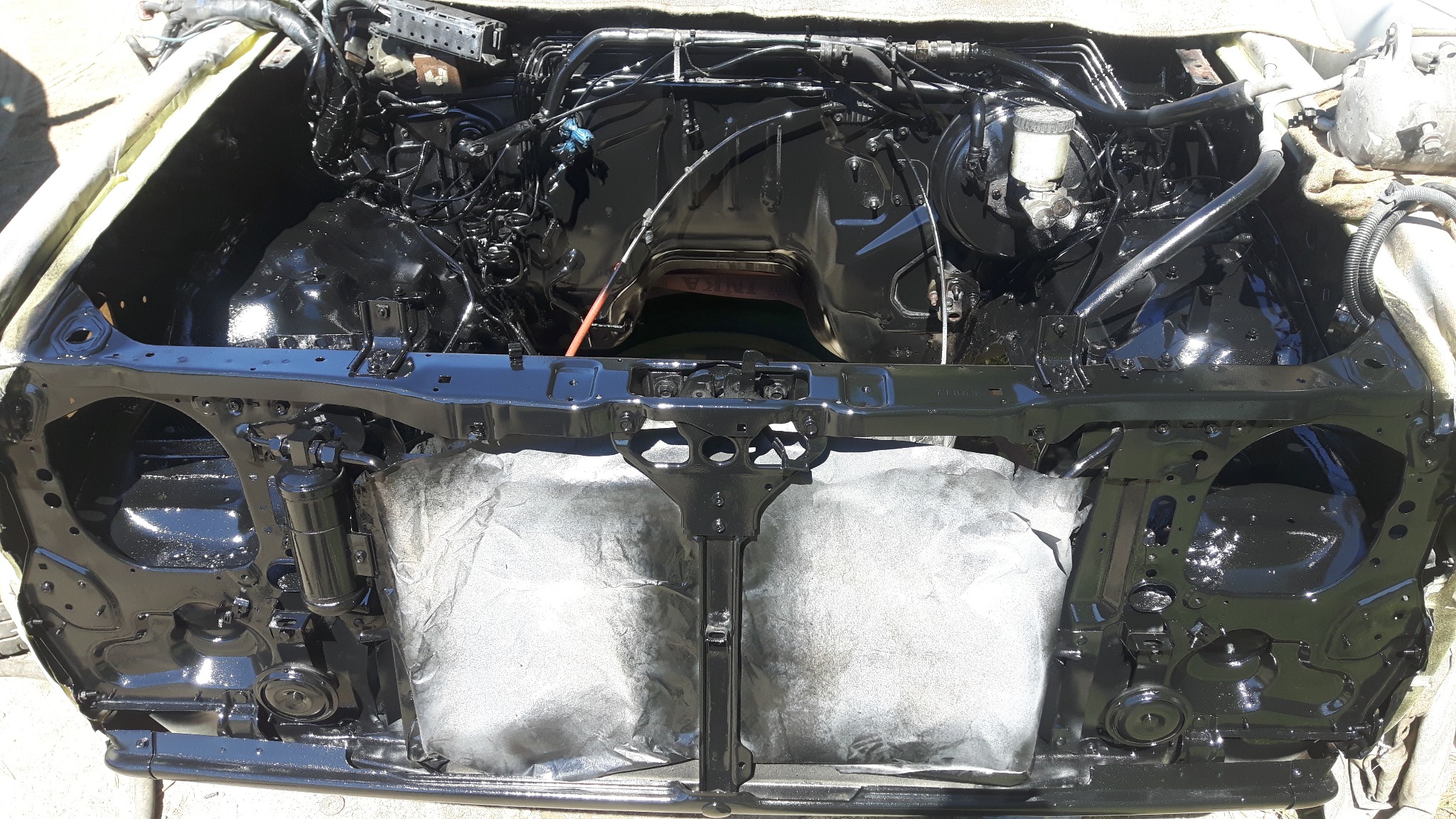 Wnętrze komory silnika samochodu po renowacji, świeżo pomalowane na czarno z widocznymi elementami instalacji i osprzętu, zabezpieczone folią malarską.