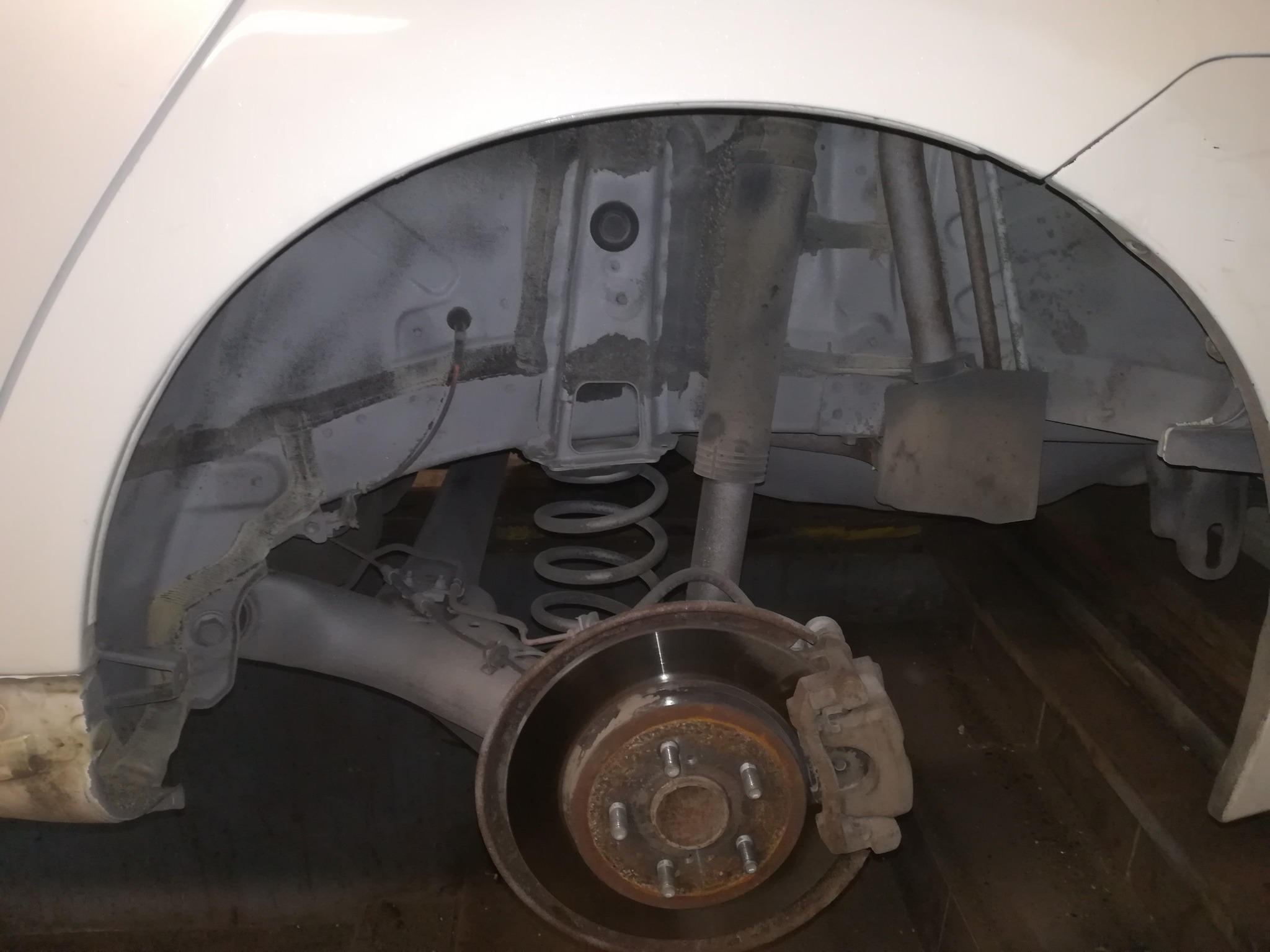 Widok na odsłonięte nadkole samochodu z widocznym zawieszeniem, sprężyną i tarczą hamulcową z zaciskiem, po prawdopodobnym oczyszczeniu i zabezpieczeniu antykorozyjnym.