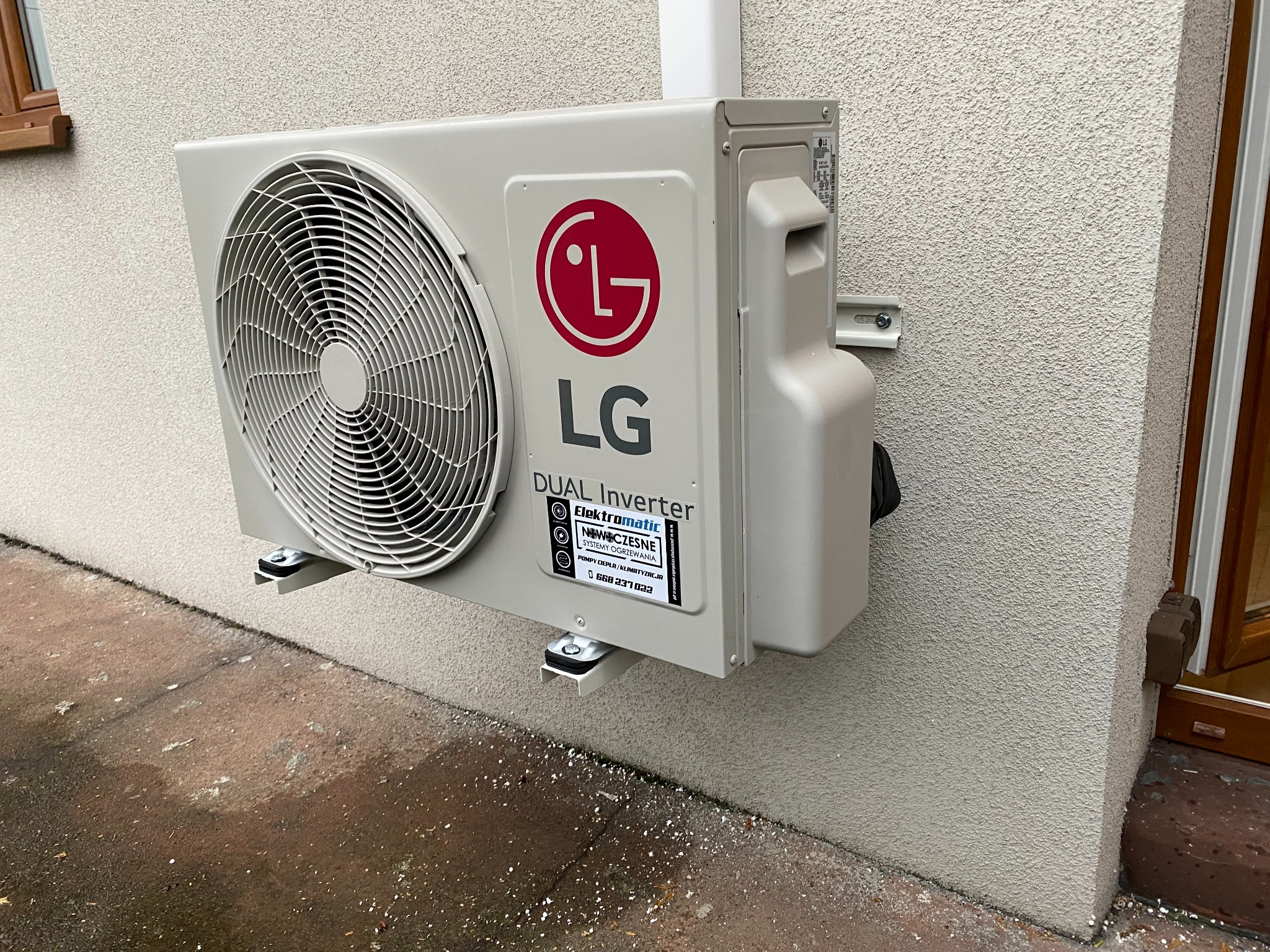 Zewnętrzna jednostka klimatyzacji LG Dual Inverter zamontowana na elewacji budynku, widoczna tabliczka reklamowa firmy instalacyjnej Elektromatic.