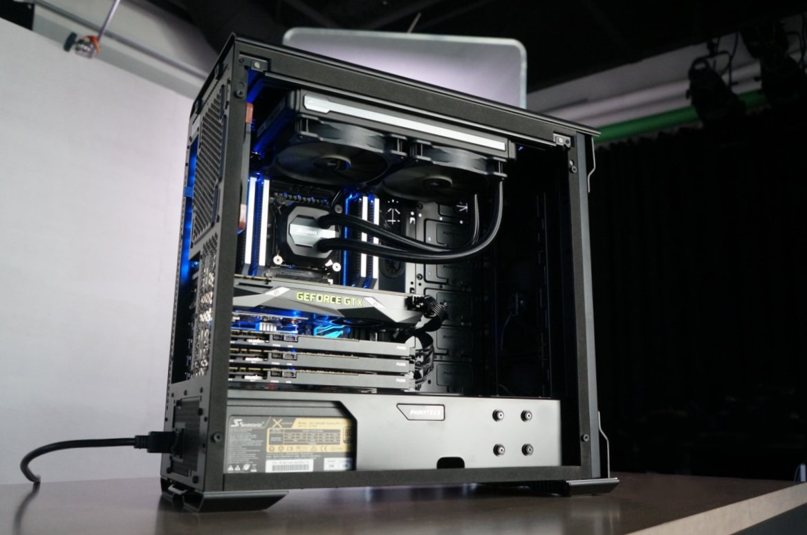 Otwarta obudowa komputera stacjonarnego z widocznym chłodzeniem wodnym, kartą graficzną GeForce GTX, pamięcią RAM z podświetleniem LED i zasilaczem Phanteks, ustawiona na stole z czarnym tłem.