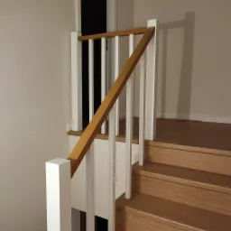 Schody drewniane z białą balustradą i drewnianą poręczą, widok z dołu, minimalistyczny design.