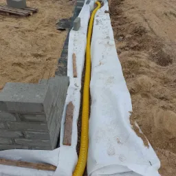 Budowa fundamentów: bloczki fundamentowe, żółta rura drenarska w geowłókninie, piasek.