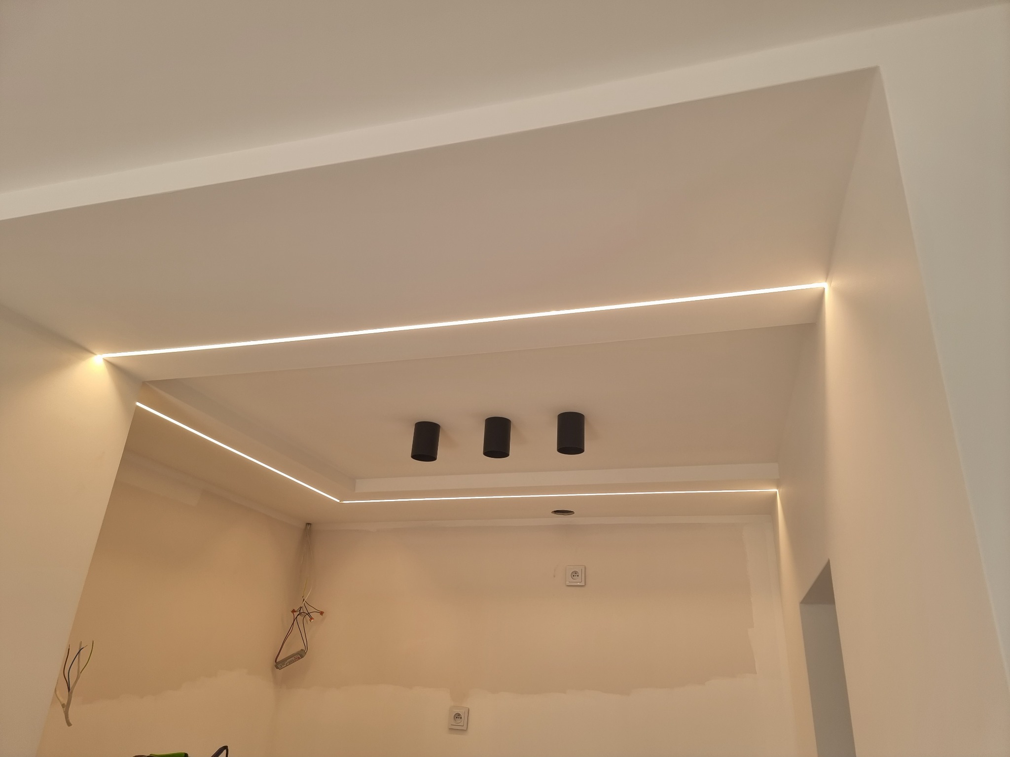 Wnętrze w trakcie remontu z widocznymi listwami LED zamontowanymi pod sufitem i trzema czarnymi lampami sufitowymi.