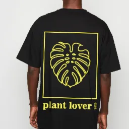 Czarny T-shirt z żółtym nadrukiem liścia monstery w kwadracie i napisem 'plant lover 2020' na plecach mężczyzny.
