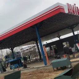 Budowa stacji benzynowej Avia w trakcie prac wykończeniowych, widoczne rusztowania, podnośnik koszowy i pracownicy układający kostkę brukową.