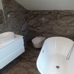 Nowoczesna łazienka z marmurowymi płytkami, białą wanną wolnostojącą, bidetem i umywalką nablatową na białej szafce z szufladami, widok z góry.