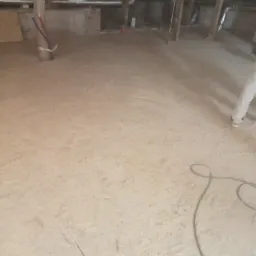 Poddasze z drewnianą konstrukcją i podłogą z płyt OSB, widoczne przewody instalacyjne przy słupie, częściowo ocieplone, w trakcie prac wykończeniowych.