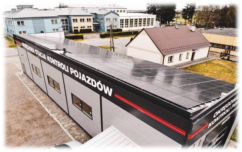 Instalacja paneli słonecznych na dachu Okręgowej Stacji Kontroli Pojazdów, widok z góry, budynki w tle.