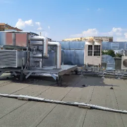 Kompleksowa instalacja wentylacyjna i klimatyzacyjna na dachu budynku, widoczne kanały wentylacyjne, klimatyzatory i rury, z elementami zabezpieczającymi przed warunkami atmosferycznymi.
