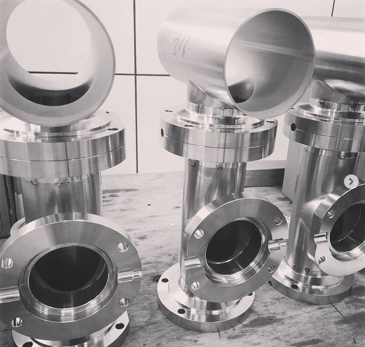 Polerowane, metalowe elementy rurowe z kołnierzami, ułożone na stole, widoczny numer '316' na jednym z elementów.