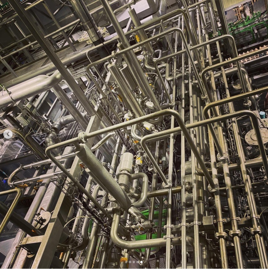 Skomplikowany system rur ze stali nierdzewnej, widok z dołu, liczne złącza i zawory, instalacja przemysłowa.
