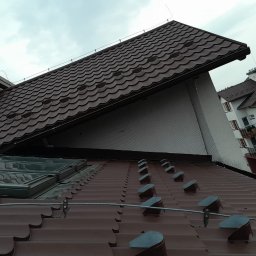 Vito Usługi Wysokościowe - Brązowy dach z dachówki ceramicznej z oknami dachowymi i systemem odgromowym, widok z góry, w tle budynek mieszkalny.