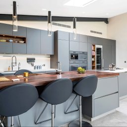 MPL Meble na wymiar - Nowoczesna kuchnia z szarymi szafkami, drewnianym blatem wyspy i designerskimi lampami. Otwarta przestrzeń, minimalistyczny styl. Widoczne sprzęty AGD i dekoracje.