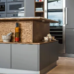 Nowoczesna kuchnia z szarymi szafkami i drewnianym blatem, oświetleniem LED. Na blacie moździerz, butelka z marynowanymi warzywami i zestaw do herbaty.