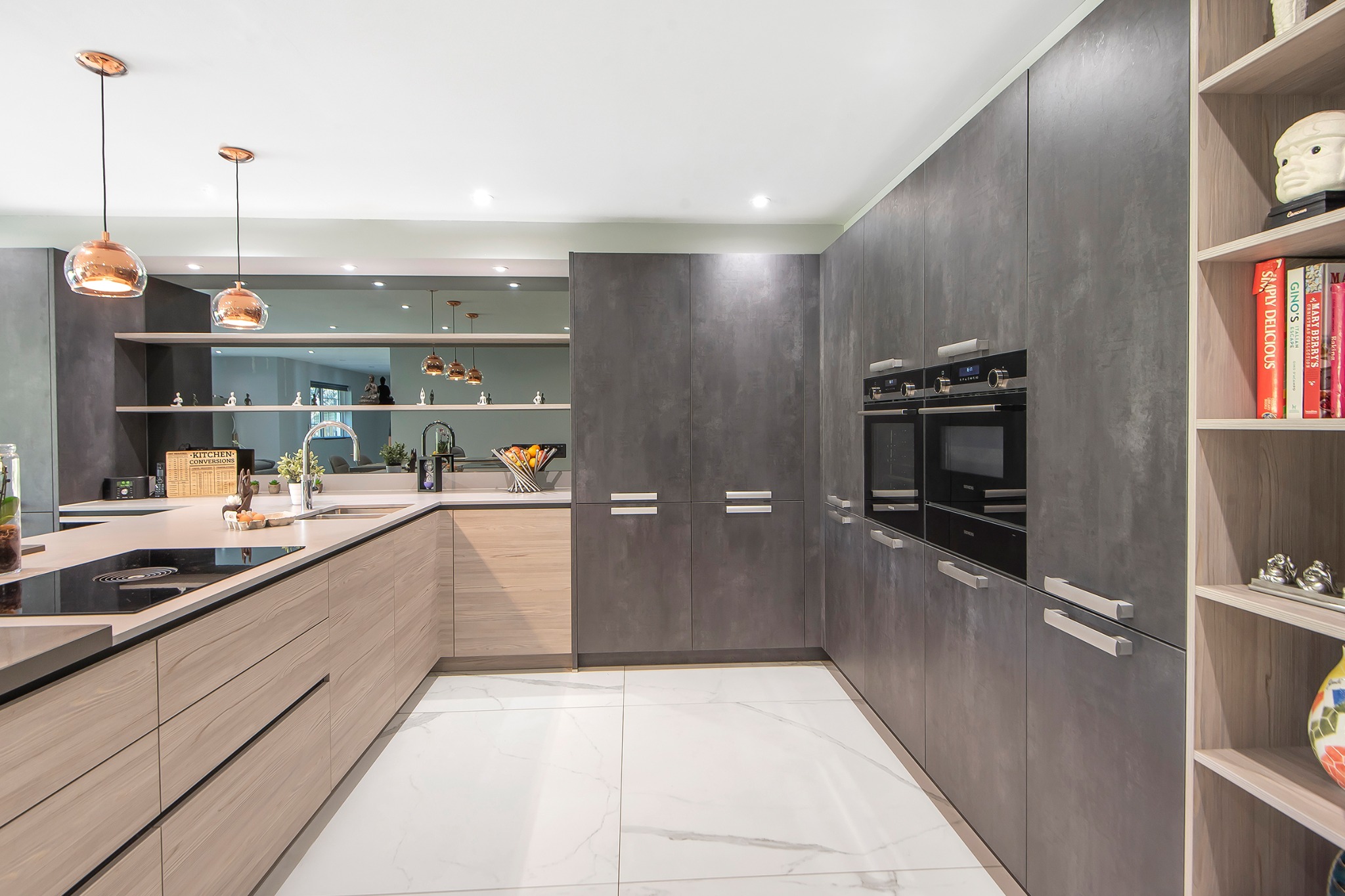 Nowoczesna kuchnia: drewniane fronty dolne, szare szafki górne, biała podłoga z marmuru. Oświetlenie punktowe i wiszące lampy miedziane.